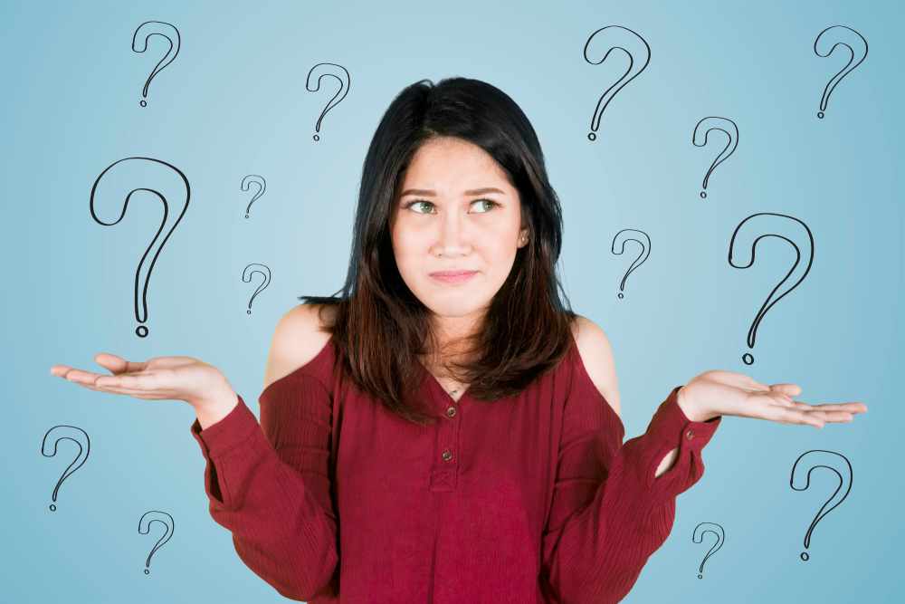A woman shrugging, with a confused look on her face, surrounded by question marks.
