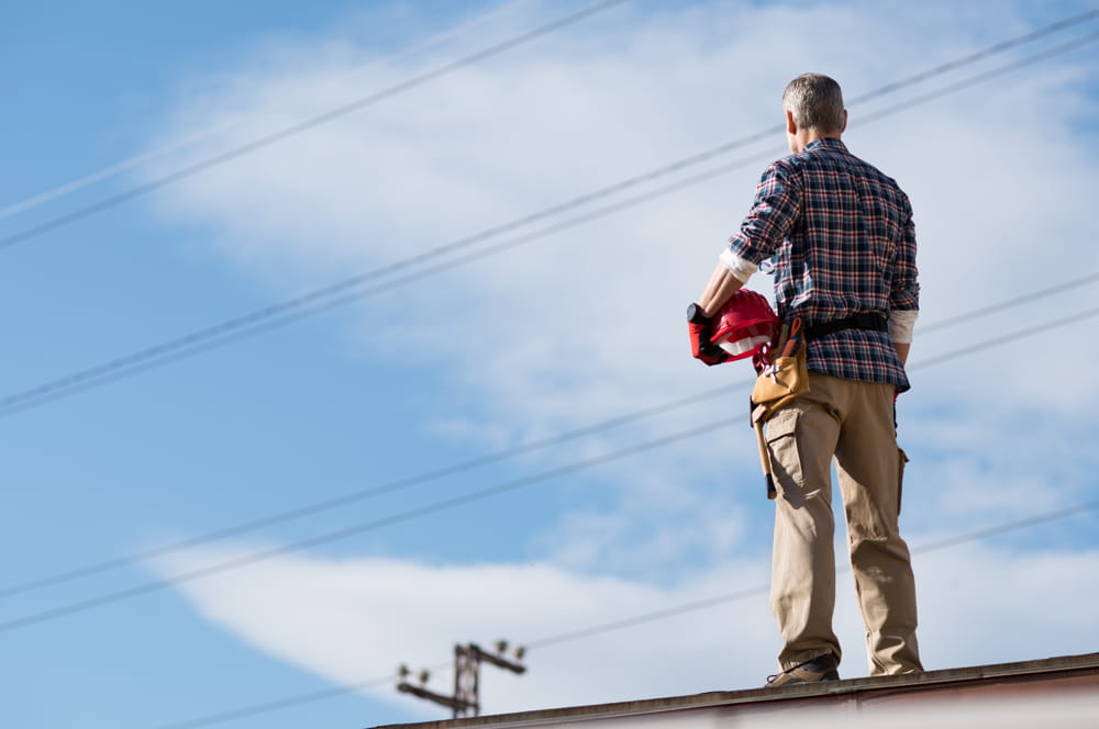 A tradesperson standing on top of a roof looking at a clear blue sky