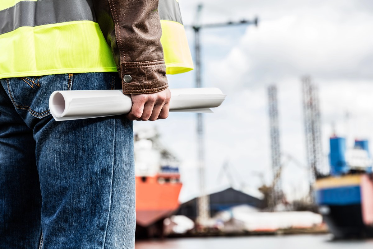 A blue collar worker standing at a job site holding documents