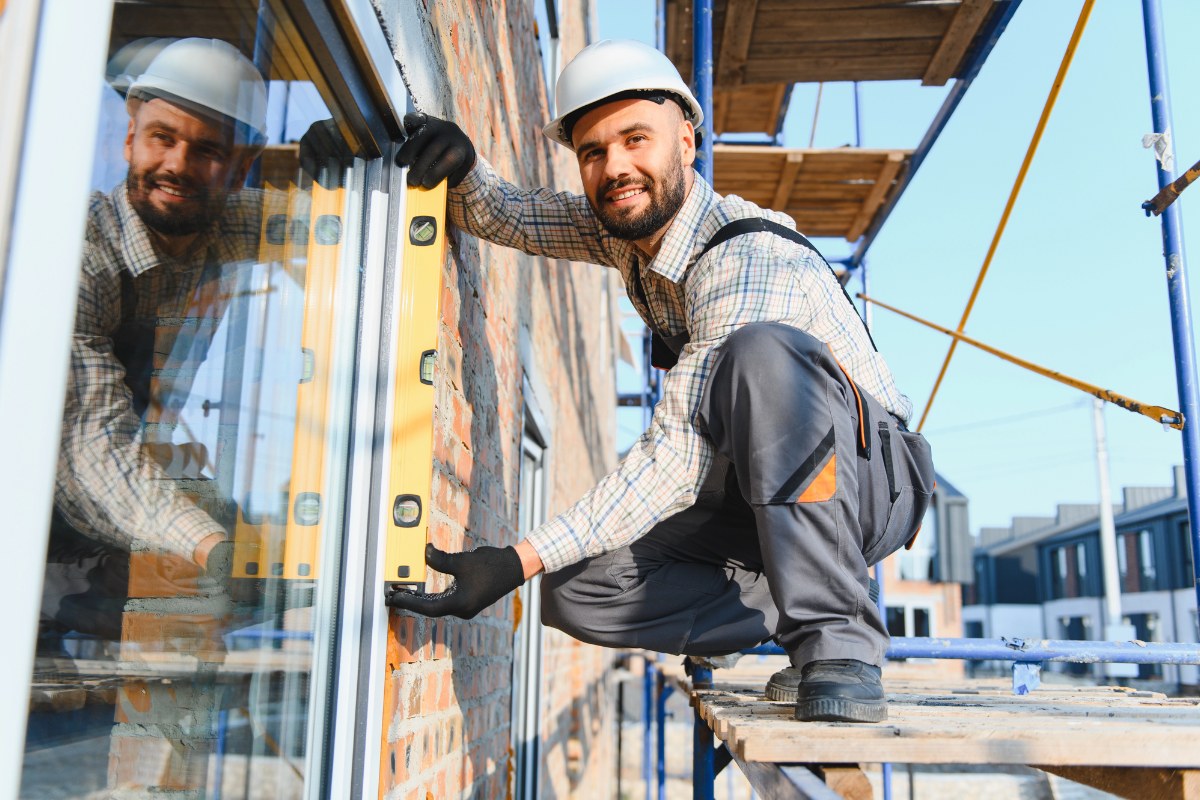 A construction worker smiling while working on windows of a building
